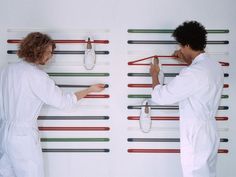 two men in white clothes are holding scissors and pointing them at something on the wall