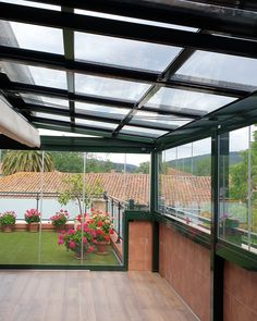 the inside of a glass enclosed patio with potted plants and flowers on the deck