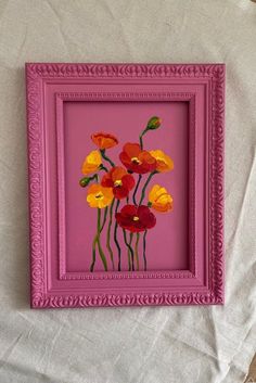 a pink frame with red and yellow flowers painted on the inside is sitting on a white sheet