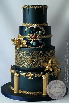 a three tiered blue and gold wedding cake with flowers on the top, surrounded by filigrees