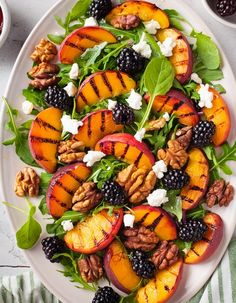 a white plate topped with grilled peaches, blackberries and walnuts on top of spinach