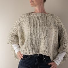 a woman standing in front of a wall with her hands on her hips wearing a sweater