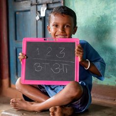 a young boy sitting on the ground holding up a chalk board with numbers written on it