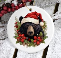 a christmas ornament with a black bear wearing a santa hat and holly berries