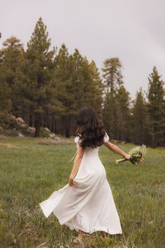 a woman in a white dress is walking through the grass with her hands behind her back