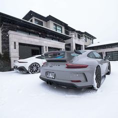 two porsches parked in front of a house on a snow covered driveway with their doors open