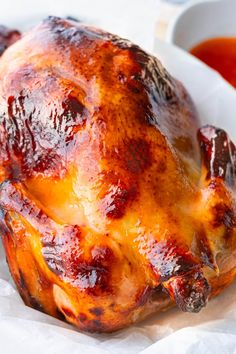 a cooked chicken sitting on top of a white plate next to a bowl of sauce