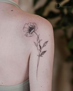 a woman's back shoulder with a single flower tattoo on her left upper arm