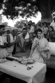 black and white photograph of people gathered around a table with food on it, in front of them