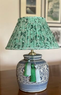 a blue and white vase with a green lamp shade on it's side sitting on a table