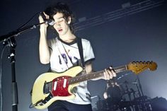 a young man holding a guitar while standing in front of a microphone