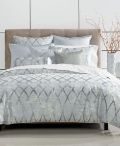 a bed with white and grey comforters in a room next to a vase filled with flowers