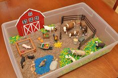 a toy farm with animals and hay in a plastic container on the floor next to a wooden table