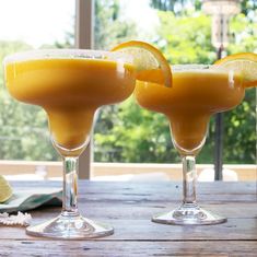 two glasses filled with orange juice and garnished with lemon wedges on a wooden table