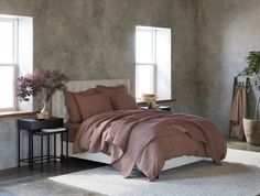 a bed with pink comforter and pillows in a room next to two large windows