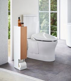 a white toilet sitting on top of a tiled floor next to a tall wooden cabinet