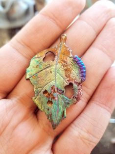 a person holding a leaf shaped pendant in their hand