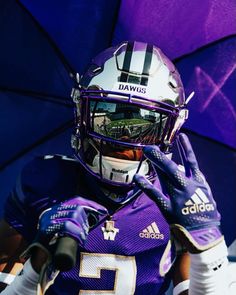 a football player wearing a purple uniform and holding an umbrella in front of his face