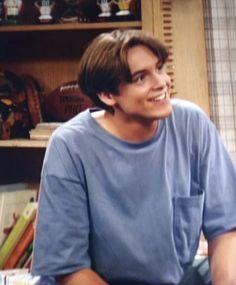 a young man sitting in front of a book shelf