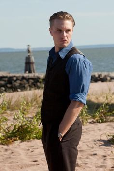 a man standing on top of a sandy beach next to the ocean with his hands in his pockets