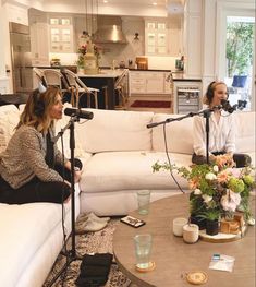 two women sitting on couches in a living room with microphones over them and flowers