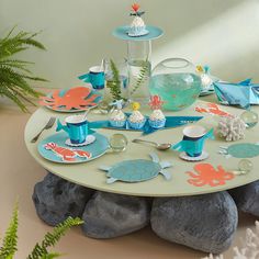 an ocean themed table setting with cupcakes, plates and cups on top of rocks