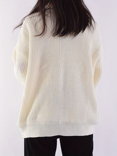 the back view of a woman wearing a white sweater and black pants, with her hands in her pockets