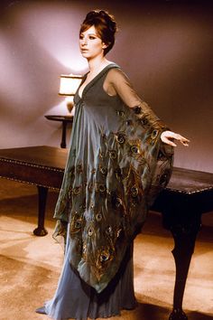 a woman standing in front of a piano wearing a dress with peacock feathers on it