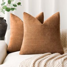 two brown pillows sitting on top of a white couch next to a potted plant