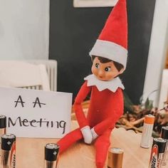 an elf sitting on top of a table next to batteries and a sign that says aa meeting