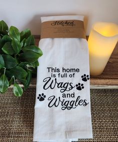 this home is full of wags and wiggles tea towel on a table next to a candle