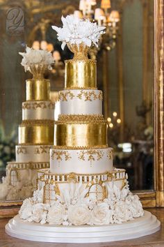 a three tiered wedding cake with white flowers on top and gold trimmings