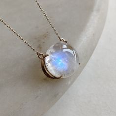 "ITEM DESCRIPTION: >>The pendant is made from Solid 14K Yellow Gold. Gemstone used is absolutely natural and ethically sourced.  >>Natural Rainbow Moonstone in Cabochon round shape with a beautiful blue sheen in prong setting is studded on it with utmost precision.  >>This is a minimalist design and is absolutely hassle-free and everyday jewelry.  Gem: Rainbow Moonstone Gem size: 15x15mm round  Gem weight: 11.80 carats Gold purity: 14K (58.33% approx.) Gold weight: 1.48 grams  Gross weight: 3.84 grams The pendent comes with 16 \" inches adjustable chain. The Gold purity is guaranteed and it comes with authentic 14K gold hallmark. Since these Pendants are handmade, they are Nickel/Lead FREE.  CUSTOMISATION: --> The same pendant can be made with a thicker bezel as well. --> You can choose yo Moon-shaped Moonstone Jewelry In White Gold, Celestial Moonstone Cabochon Jewelry, White Gold Moon-shaped Moonstone Jewelry, Formal Moonstone Round Necklace, Formal Round Moonstone Necklace, Moonstone Round Necklace For Anniversary, Celestial Moonstone Round Pendant Jewelry, Celestial Moonstone Gemstone Necklace, Moonstone Round Pendant Jewelry For Anniversary