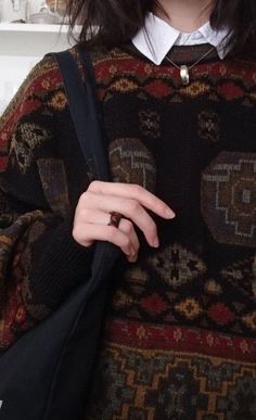 a close up of a person wearing a sweater and holding a bag with her hand