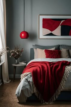 a bed in a bedroom with a red blanket on top of it and a painting hanging above the bed