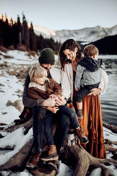 a group of people sitting next to each other on top of a tree stump in the snow