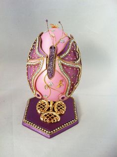 a pink and gold egg with jewels on it's head sitting on a stand