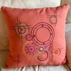 a pink pillow on a white couch with embroidered circles and lines around the edges,