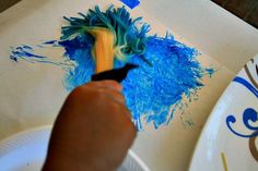 a person is painting with blue paint on a white plate and holding a yellow brush