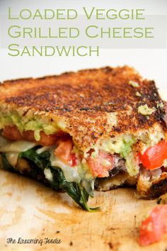 a grilled cheese sandwich on a cutting board with tomatoes and spinach in the middle