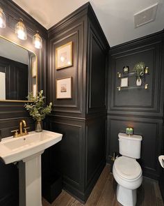 a white toilet sitting next to a sink in a bathroom under two framed pictures on the wall