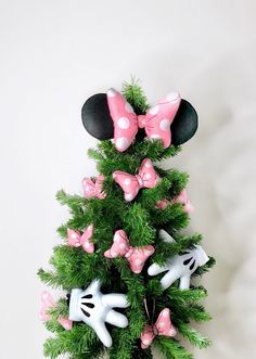 a minnie mouse christmas tree with pink and white bows on it's head, sitting in front of a white wall