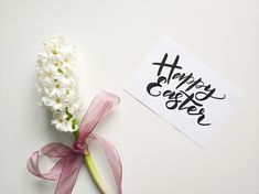 a white flower with a pink ribbon next to a piece of paper that says happy easter