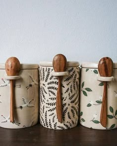 four wooden spoons are lined up next to each other in ceramic containers with designs on them