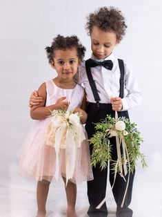 two young children dressed in tuxedos and bow ties, one holding a bouquet