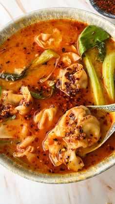 a bowl filled with pasta and vegetables on top of a wooden table next to a spoon