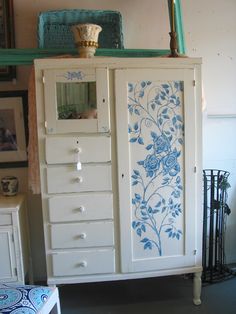 a white cabinet with blue flowers painted on the doors and drawers, in a living room