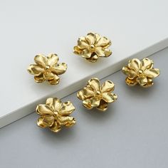 three pieces of gold - plated metal flowers on a white surface, with one flower in the middle