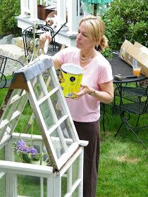 a woman holding a yellow cup in front of a white ladder with flowers growing out of it