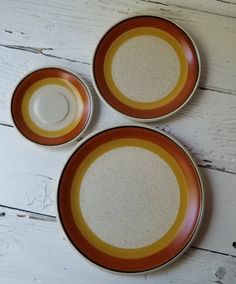 three orange and white plates sitting on top of a wooden table